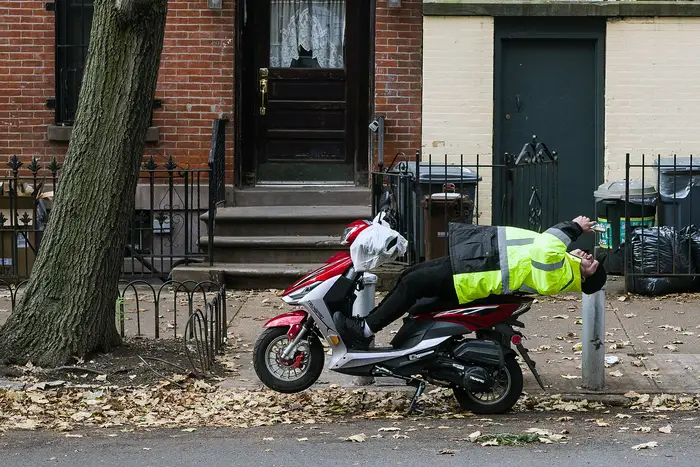 a delivery worker on a vespa outside a townhouse